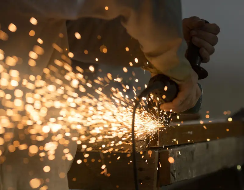 Worker using an angle grinder on metal, with sparks spraying across the work surface.