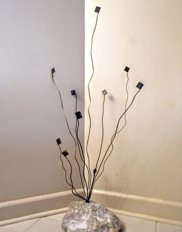 Indoor welded metal sculpture with thin curved rods and square tips mounted on a stone base.