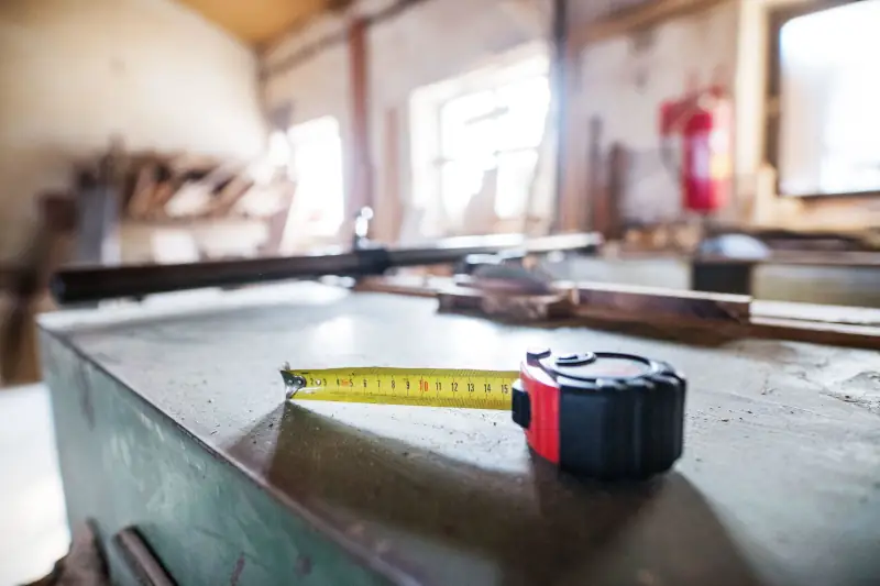 Tape measure on a metal workbench in a fabrication shop, with tools blurred in the background.